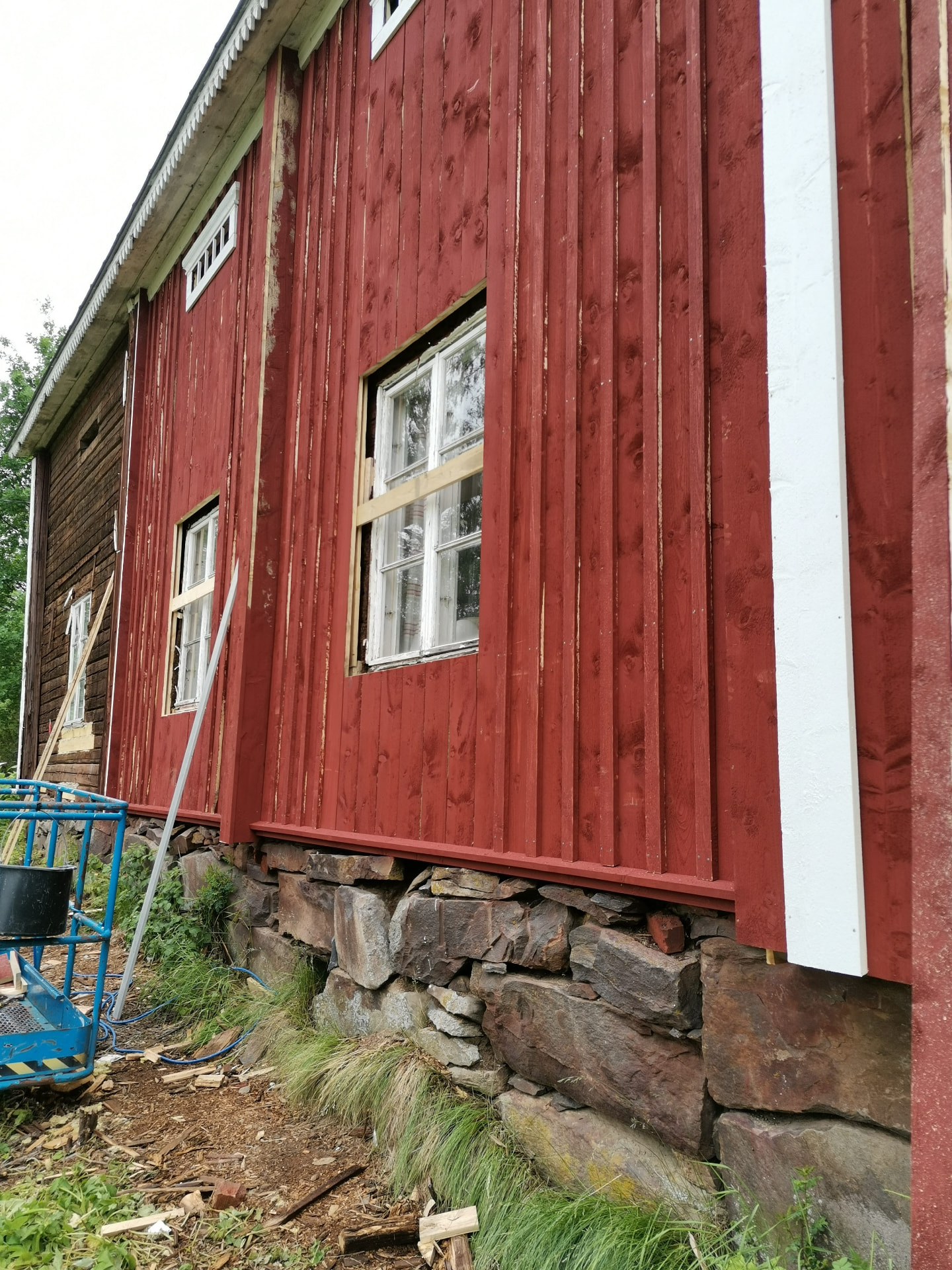 Vanhan punaisen puutalon ulkoverhouksen korjaustyö kivijalan päällä